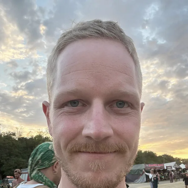 Jan lächelt in die Kamera, im Abendlicht auf einem Festivalgelände